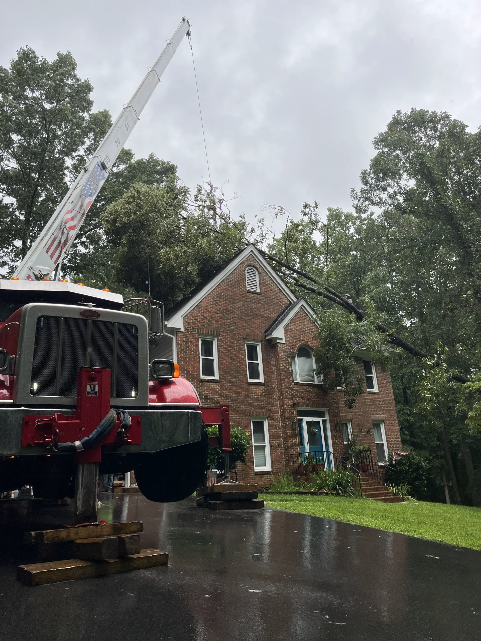Fonvilletreeservice crane truck removing large fallen tree from residential brick home roof during storm cleanup in NC