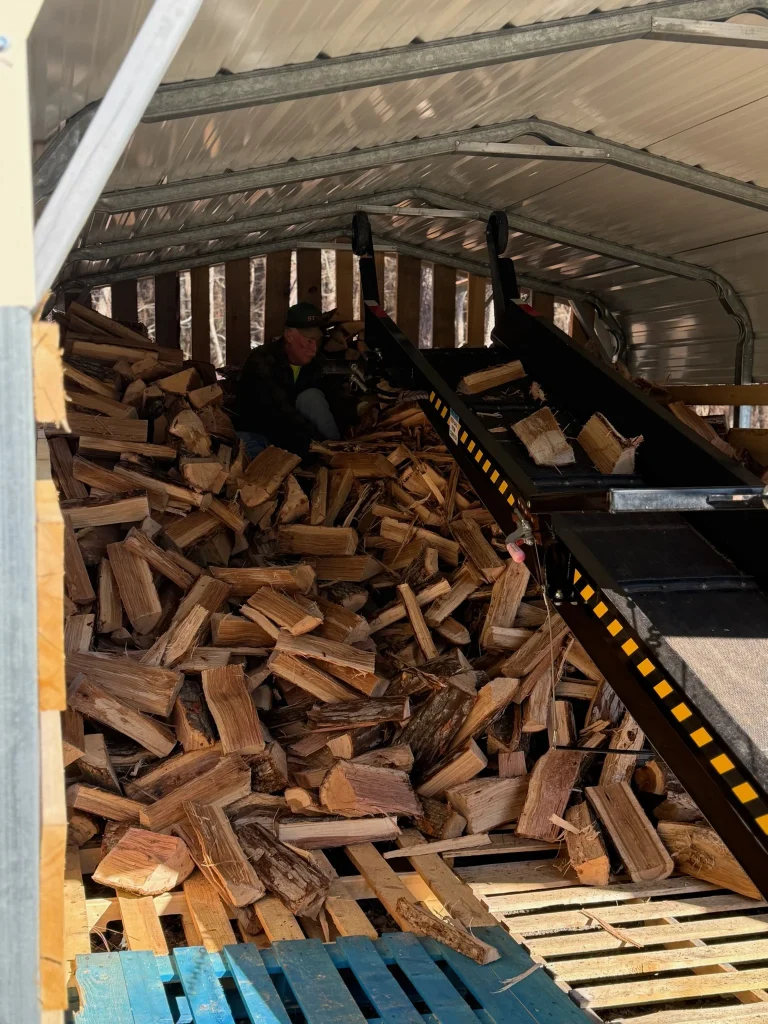 Fonvilletreeservice worker loading split firewood onto conveyor belt inside covered storage facility in NC