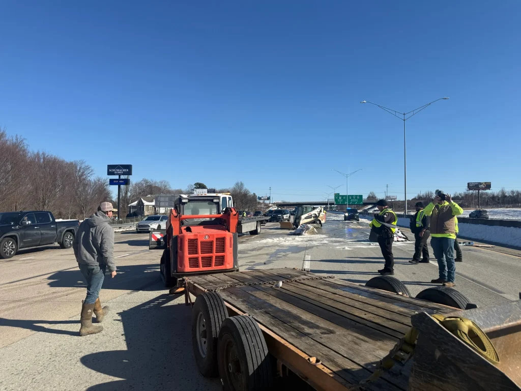 Fonvilletreeservice crew operating red skid steer loader clearing snow from highway with flatbed trailer and workers in safety vests NC