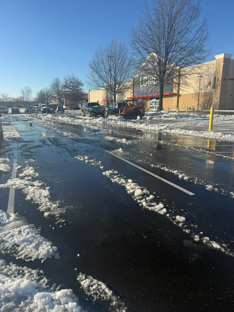 Fonvilletreeservice crew clears melting snow and slush from wet commercial parking lot using orange skid steer equipment in NC