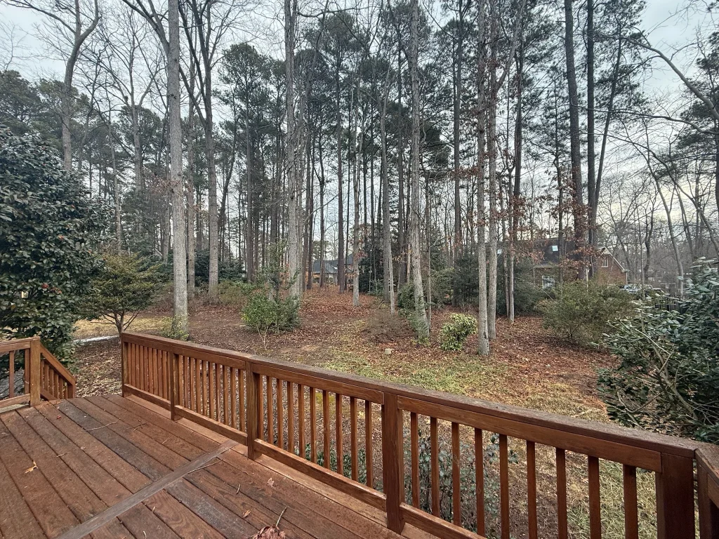 Fonvilletreeservice wooded residential backyard view from stained wooden deck showing mature pine trees and leaf-covered ground in NC.