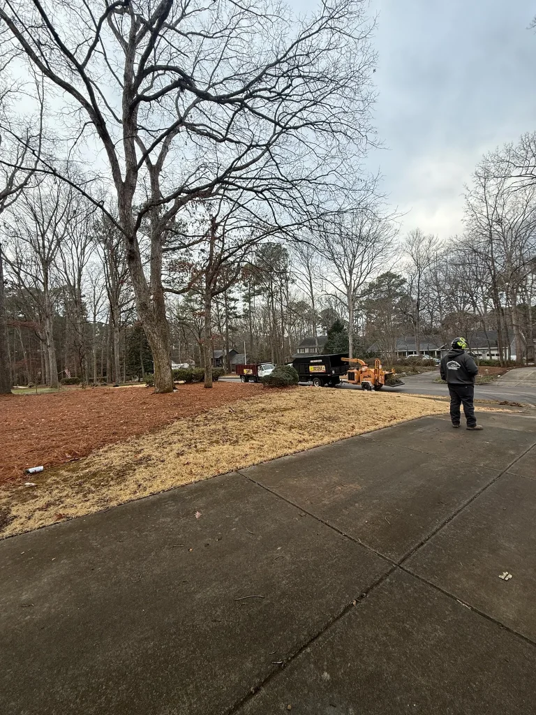 Fonvilletreeservice crew member observing wood chipper and dump trailer setup on suburban residential street in NC during winter service.