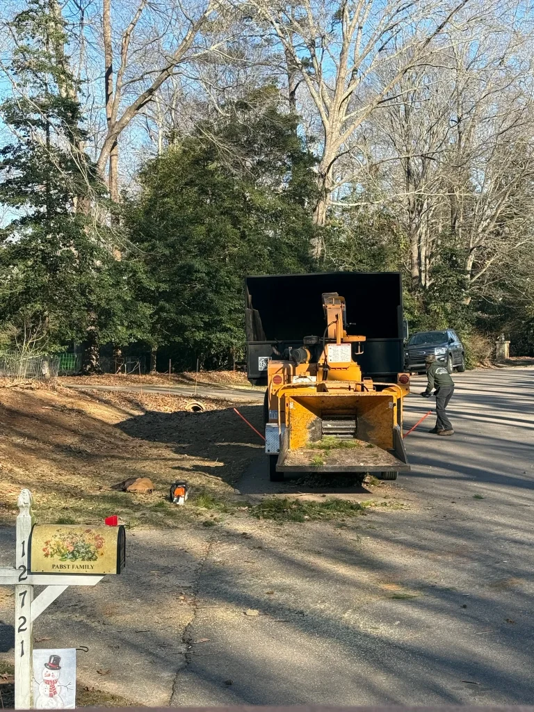 Fonvilletreeservice crew member feeding branches into orange wood chipper with dump trailer at residential property in NC