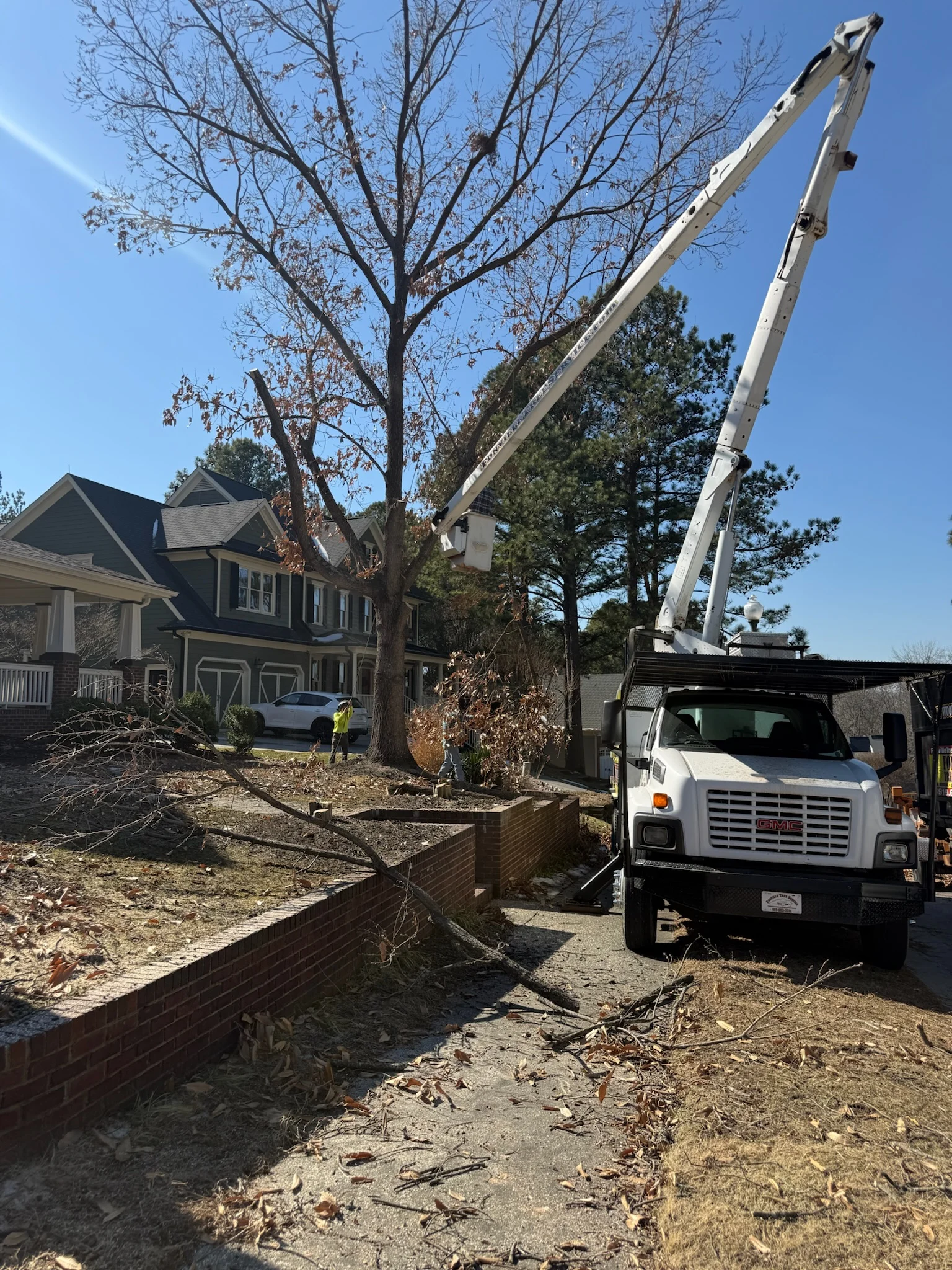 Fonvilletreeservice crew operating white bucket truck crane to remove large deciduous tree near residential home in NC