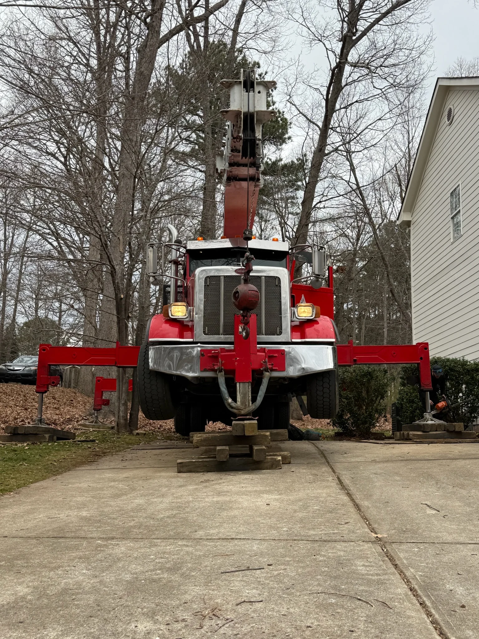 Home 5 Fonvilletreeservice red crane truck with outriggers deployed and stabilized on wooden cribbing in residential driveway NC